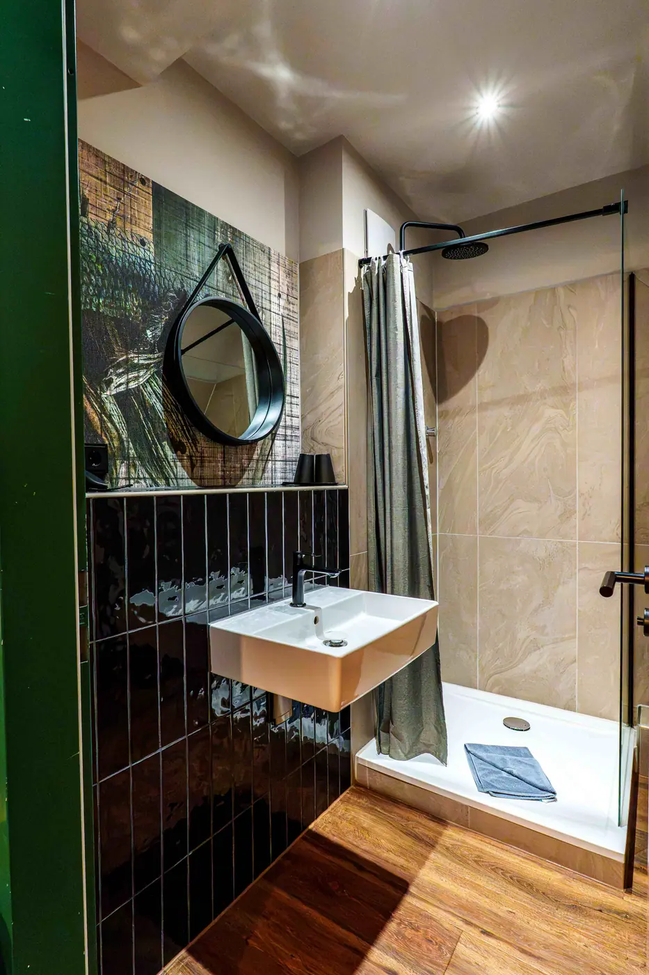 Badezimmer mit rundem Spiegel, schwarzen Fliesen, Waschbecken und Dusche