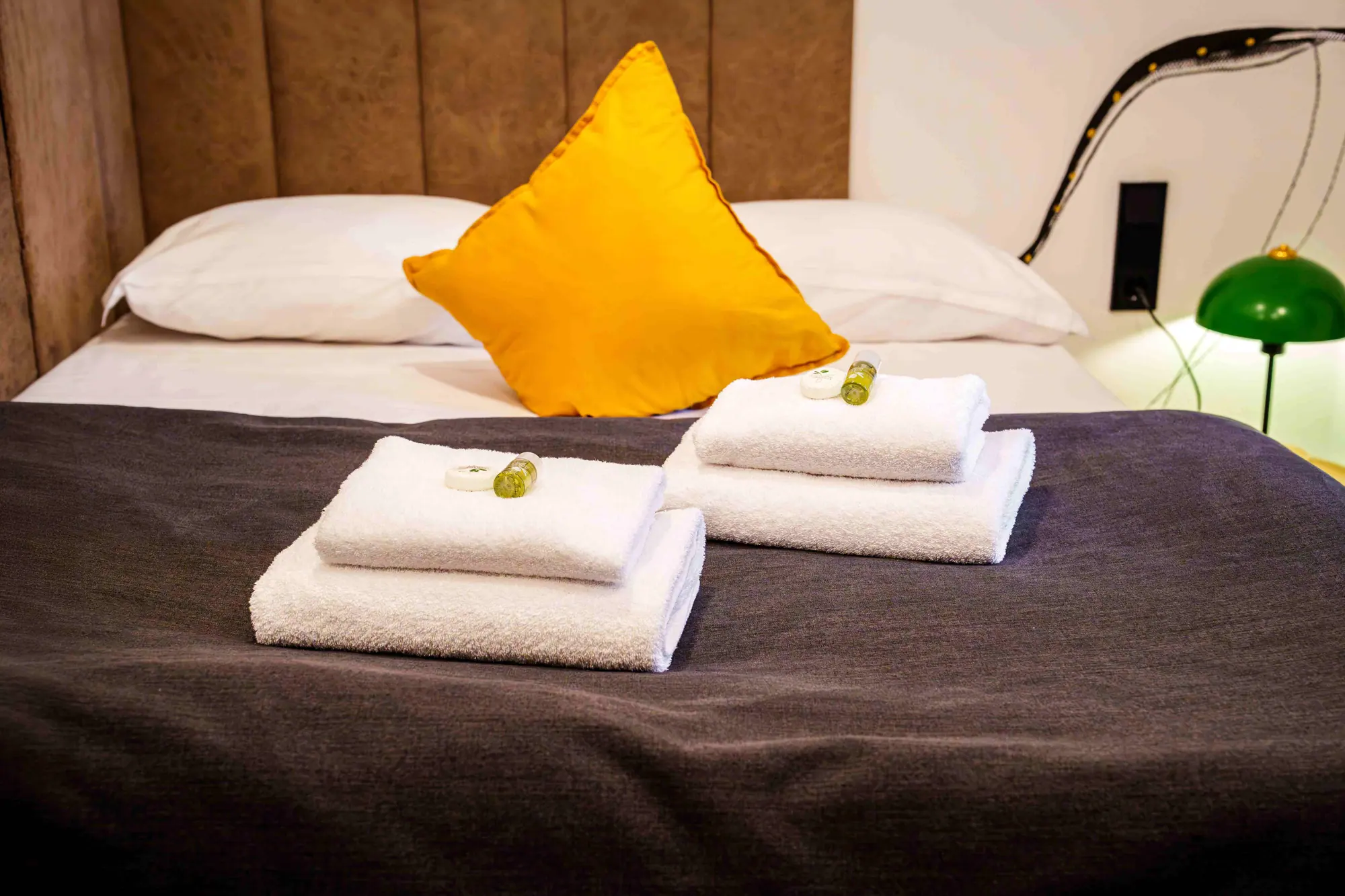 Bett mit Handtüchern, gelbem Kissen und grüner Leuchte im Mezzotel