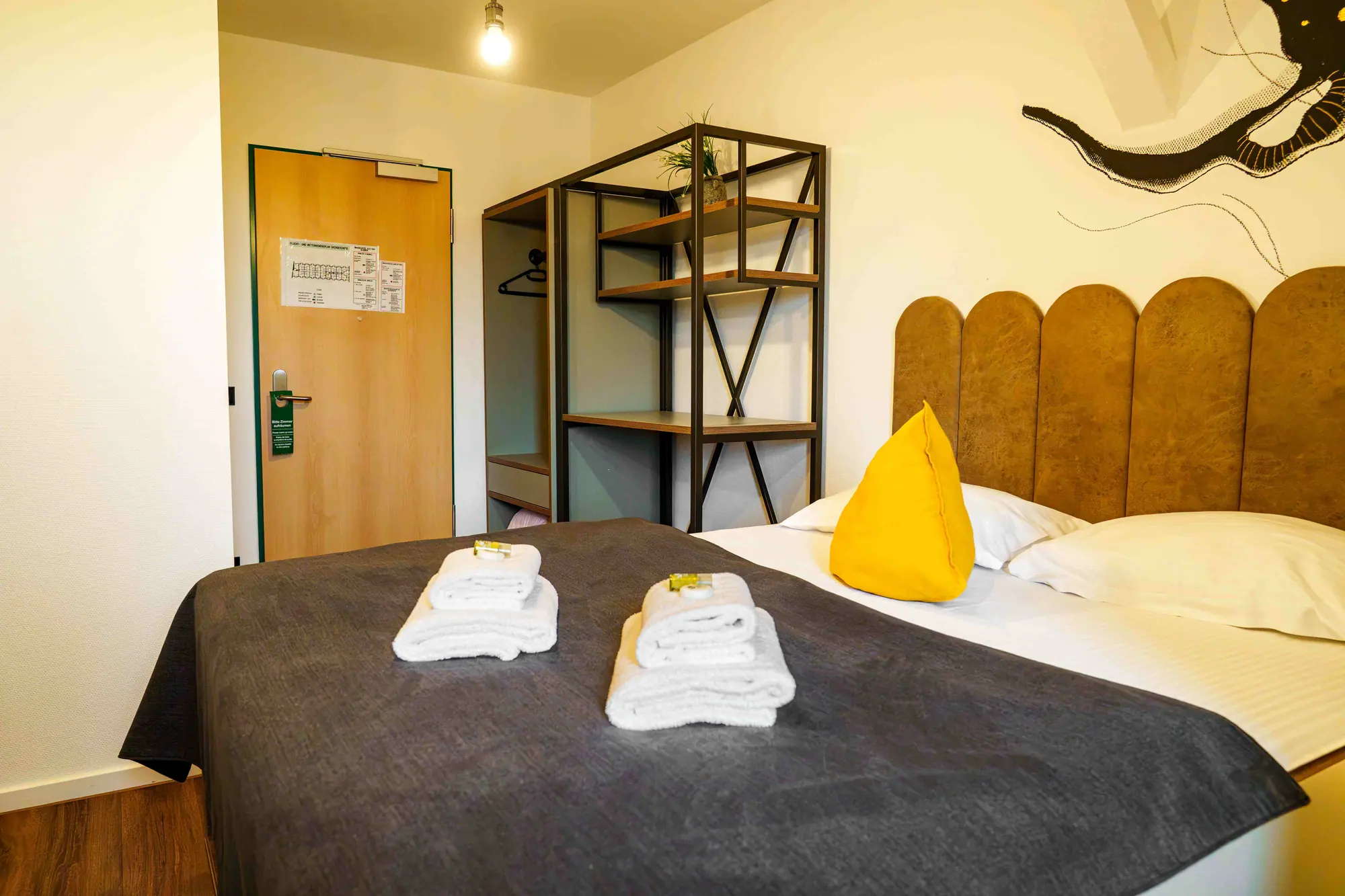 Doppelbett mit Handtüchern, Metall-Garderobe und Zimmertür im Mezzotel