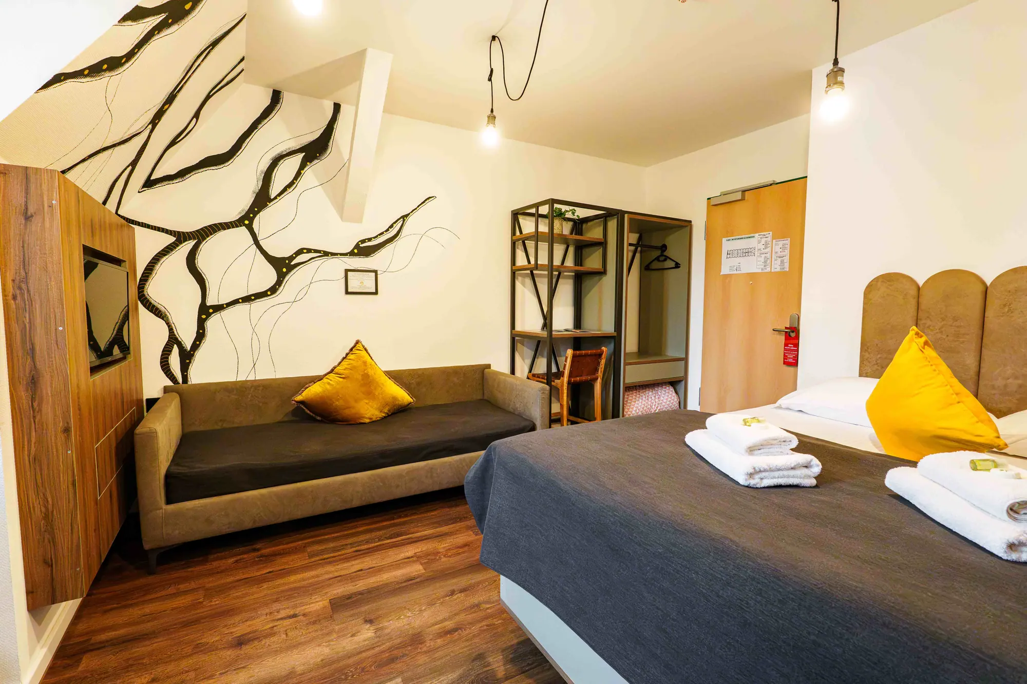 Mezzotel Zimmer mit Doppelbett, Sofa, TV-Paneel und Wandlinien
