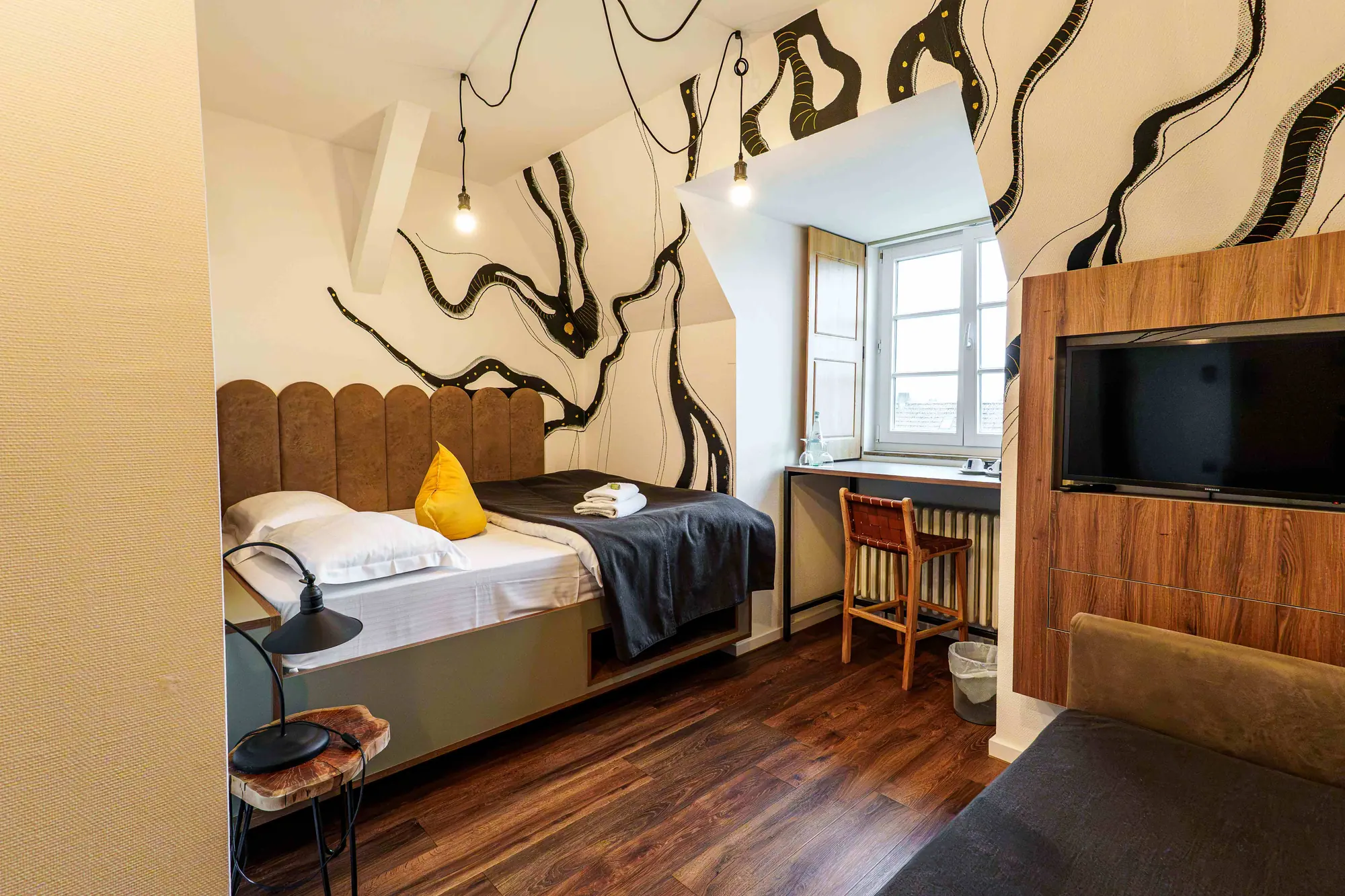 Mezzotel Zimmer mit Bett, Polsterkopfteil, Fensterplatz mit Barhocker und Wandkunst