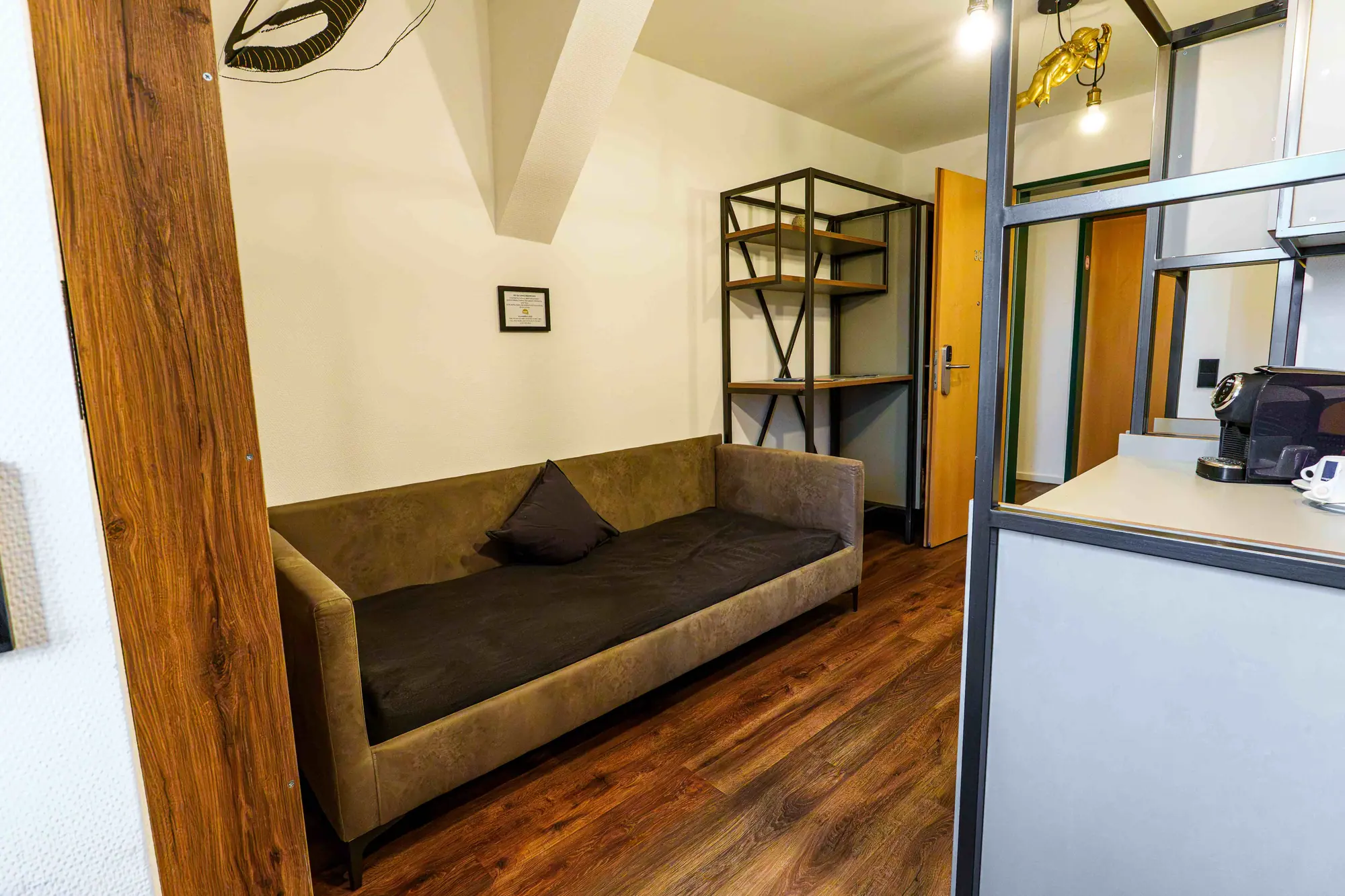 Eingangsbereich eines Mezzotel Zimmers mit Sofa, Regal und Teeküche